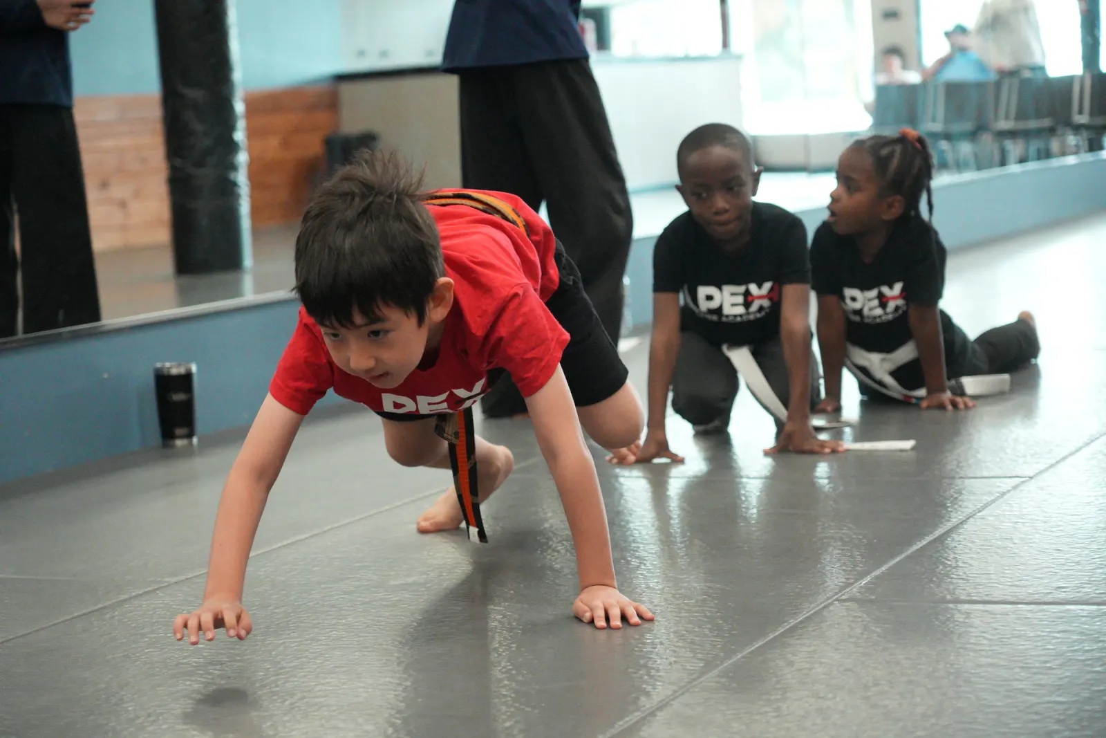Student in a red Apex shirt on the mat during a drill