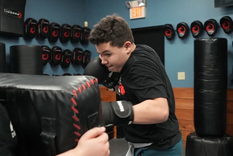 Teen in gloves punching a held pad